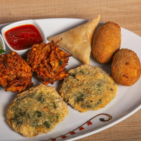 A platter of Indian appetizers including samosas, pakoras, and other fried snacks with dipping sauces.