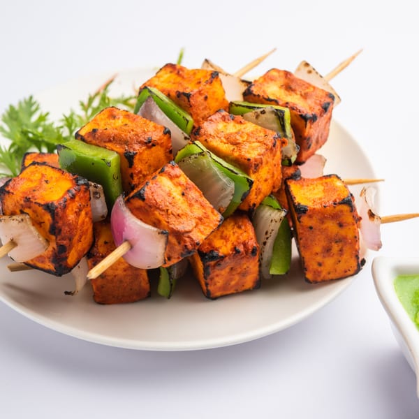 Rasoi's paneer tikka skewers with charred paneer, green peppers, and onions on a white plate.