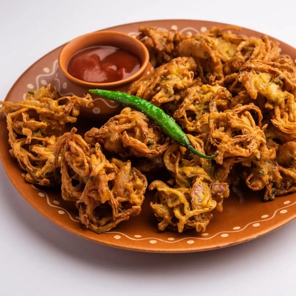 Crispy golden onion pakoras with a side of red chutney and a green chili on a brown plate.