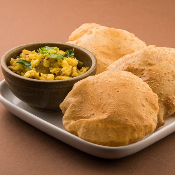 A bowl of Indian potato curry with cumin and cilantro, served with three golden-brown puri breads.